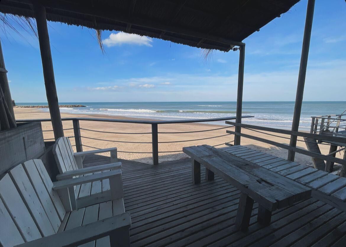 Terraza de madera con bancos que da a una playa.
