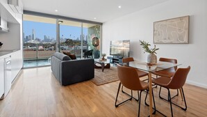Uma sala de estar moderna com uma mesa de jantar de vidro, sofá cinza e vista da cidade através de grandes janelas.