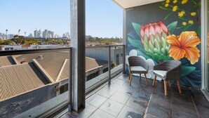 Varanda com vista para a cidade, um mural de flores e duas cadeiras de vime.