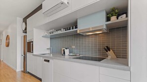 Uma cozinha moderna com armários brancos, forno embutido, máquina de lavar louça, pia e bancada com porta-facas.
