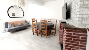 A living room with a sofa, dining table, chairs, a TV mounted on a brick wall, and a hanging light fixture. - Family Stay at Gîte Iza – Lormes, Morvan (Lormes)