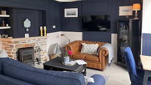 A cozy living room with a stone fireplace, a leather sofa, a blue armchair, and a television. - Cottage 492 - Clifden - sleeps 5 guests  in 3 bedrooms (Clifden)