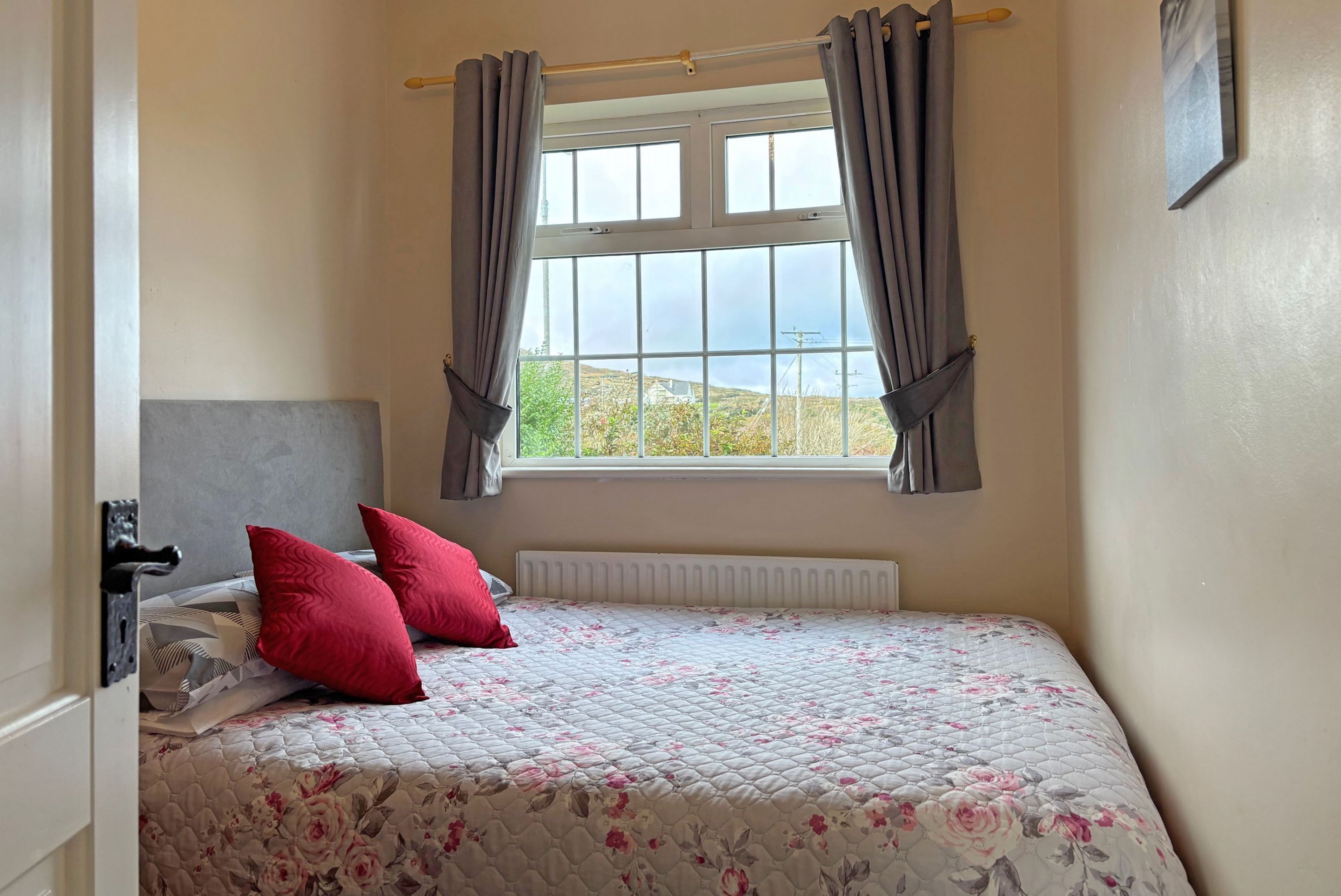 A bedroom with a bed, two red pillows, a radiator, and a window with curtains.