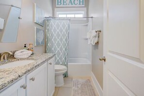 A bathroom with a sink, toilet, bathtub, and shower curtain. - Ocean-View Escape  — Steps to the Beach! (Myrtle Beach)