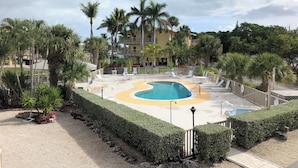 Zona de piscina en un resort, con piscina circular, palmeras y un edificio al fondo.