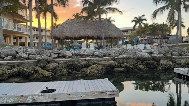 Un resort con una cabaña de techo de paja, palmeras, una piscina y un muelle.