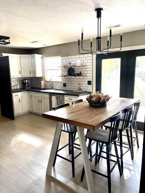 A modern kitchen with white cabinets, a wooden dining table, and a black chandelier.