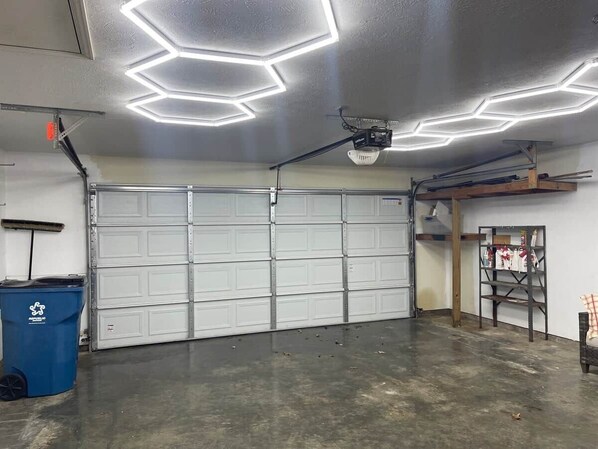 A garage with a large white door, a ceiling-mounted projector, and a blue trash bin.