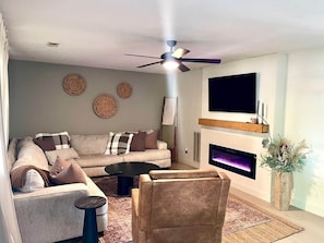 Un salon comprenant un canapé, une table basse, une cheminée, un ventilateur de plafond et un téléviseur fixé au mur.