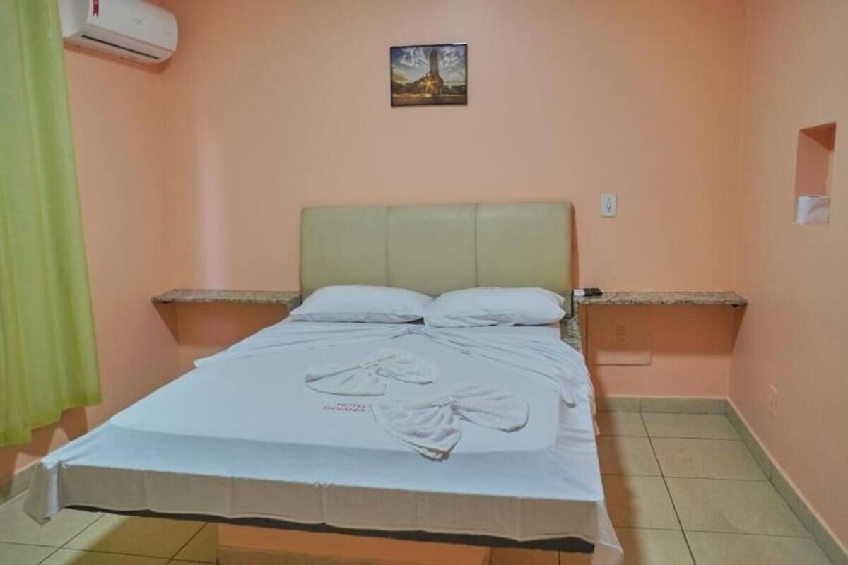 A bedroom with a bed, a green curtain, an air conditioning unit, and a small painting on the wall.