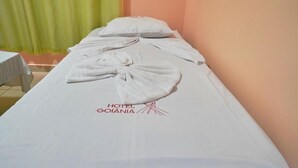 A hotel room with a neatly made bed, a pillow, and a towel arranged on the bed. The room has a simple layout with a plain wall and a curtain in the background. - Hotel Goiânia (Goiânia)