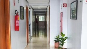 A clean, well-lit hallway with tiled floors, wooden doors, and potted plants. - Hotel Goiânia (Goiânia)