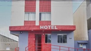A hotel with a red and white facade, a visible entrance, and a parking area in front. - Hotel Goiânia (Goiânia)