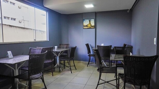 A room with a large window, several tables and chairs, and a framed picture on the wall. - Hotel Goiânia (Goiânia)