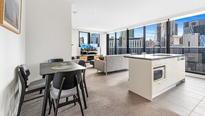 A modern apartment with a dining area, kitchen, and large windows offering city views. - Pristine 2-Bed Unit With Beautiful City Landscape (Southbank)