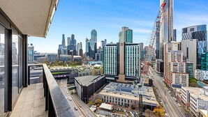 A cityscape with modern high-rise buildings, a construction crane, and a busy street below. - Pristine 2-Bed Unit With Beautiful City Landscape (Southbank)