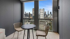 Un balcon avec vue sur la ville, deux fauteuils en osier, une table ronde et une boîte blanche portant l’inscription « Fuji ».
