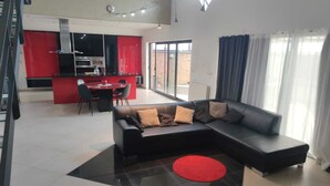 Uma sala de estar moderna com um sofá seccional, uma área de jantar e uma cozinha com armários vermelhos.