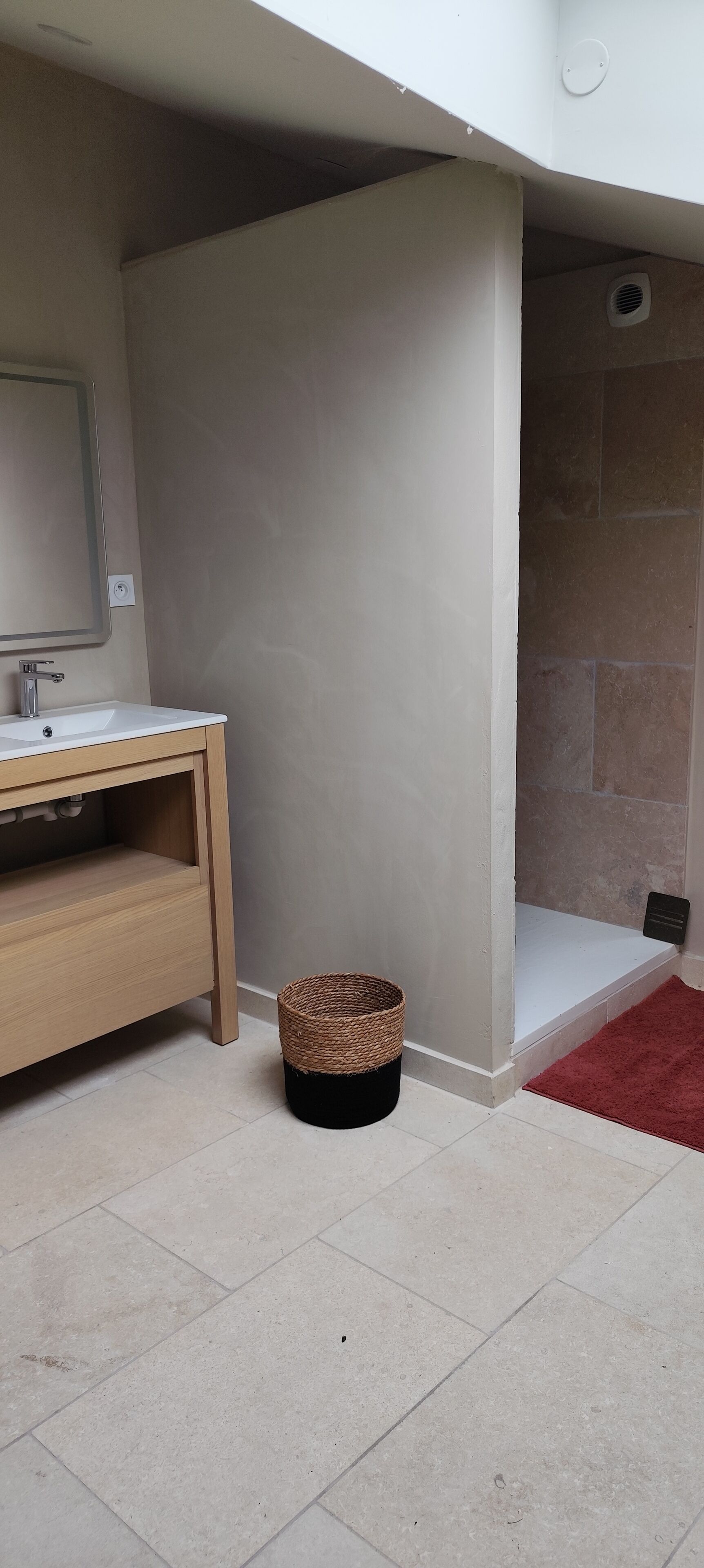 A bathroom with a wooden vanity, a small wicker basket, and a red rug.