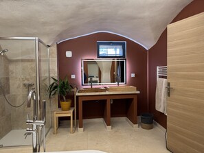 A bathroom with a glass shower enclosure, a wooden vanity with a mirror, a potted plant, and a towel rack.