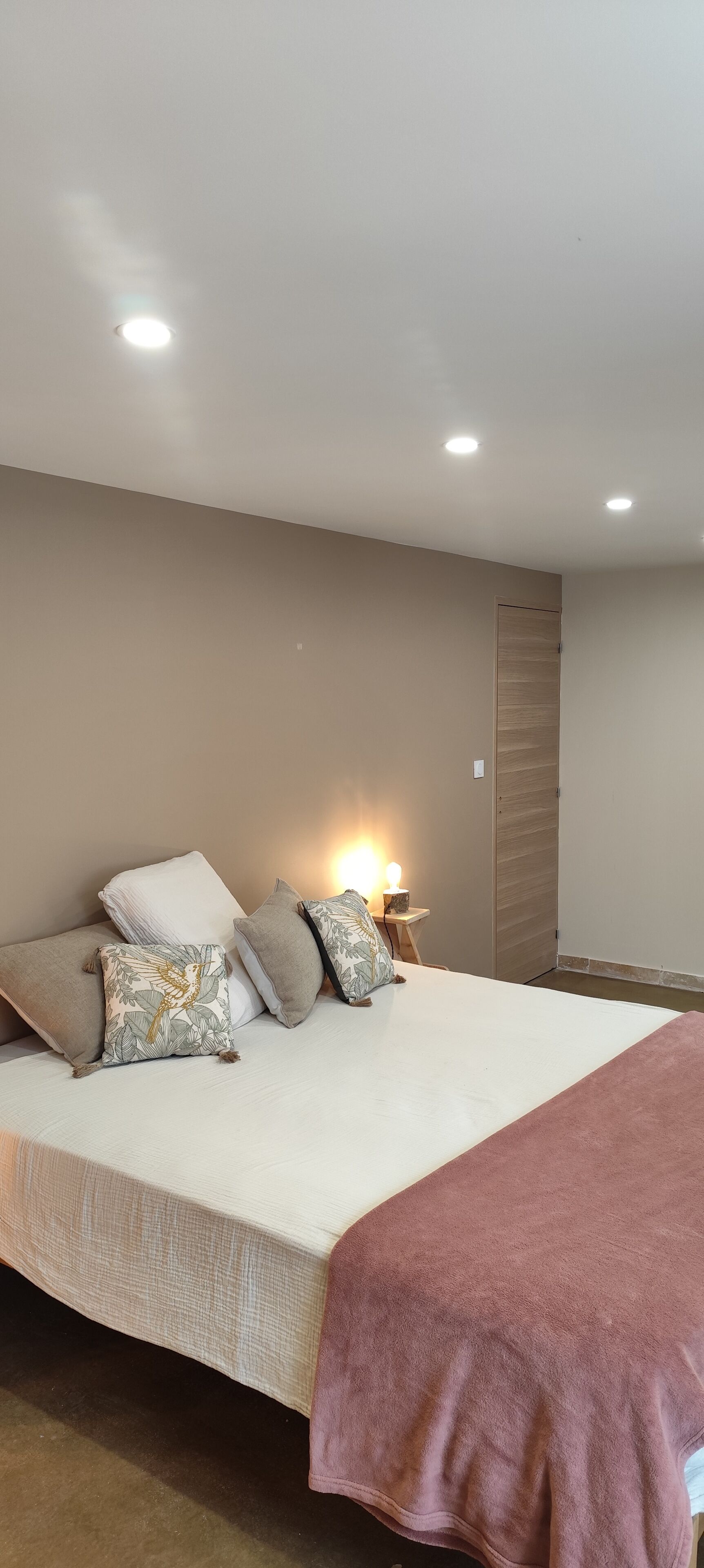 A bedroom with a bed, pillows, a bedside table with a lamp, and a wooden wardrobe.