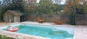 A rectangular swimming pool with a stone wall and two wooden loungers.