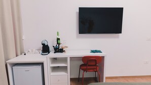 A compact room with a white desk, a small refrigerator, a red chair, and a bed. - La Tana del Furlo (Cagli)