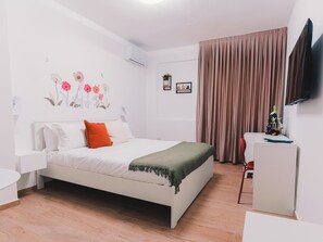 A bedroom with a bed, a desk, a chair, a television, and a wall with floral decorations. - La Tana del Furlo (Cagli)
