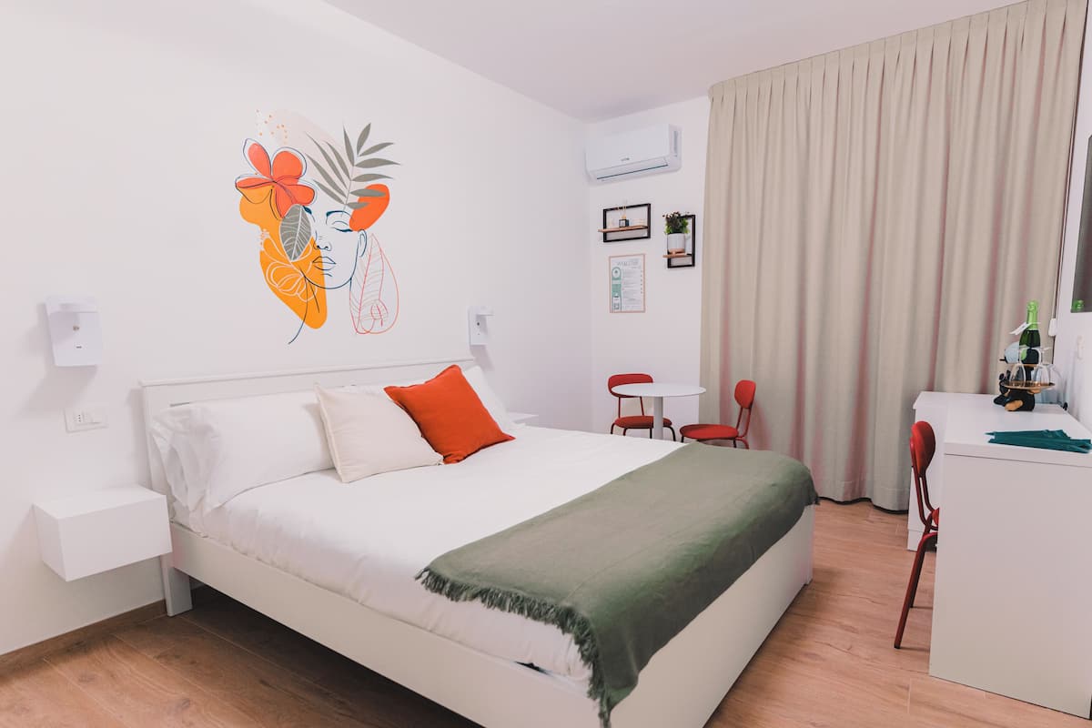Una habitación de hotel con cama, escritorio, silla, aire acondicionado instalado en la pared y cortina.
