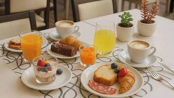A breakfast setting with croissants, a sandwich, a dessert, coffee, and juice on a table.