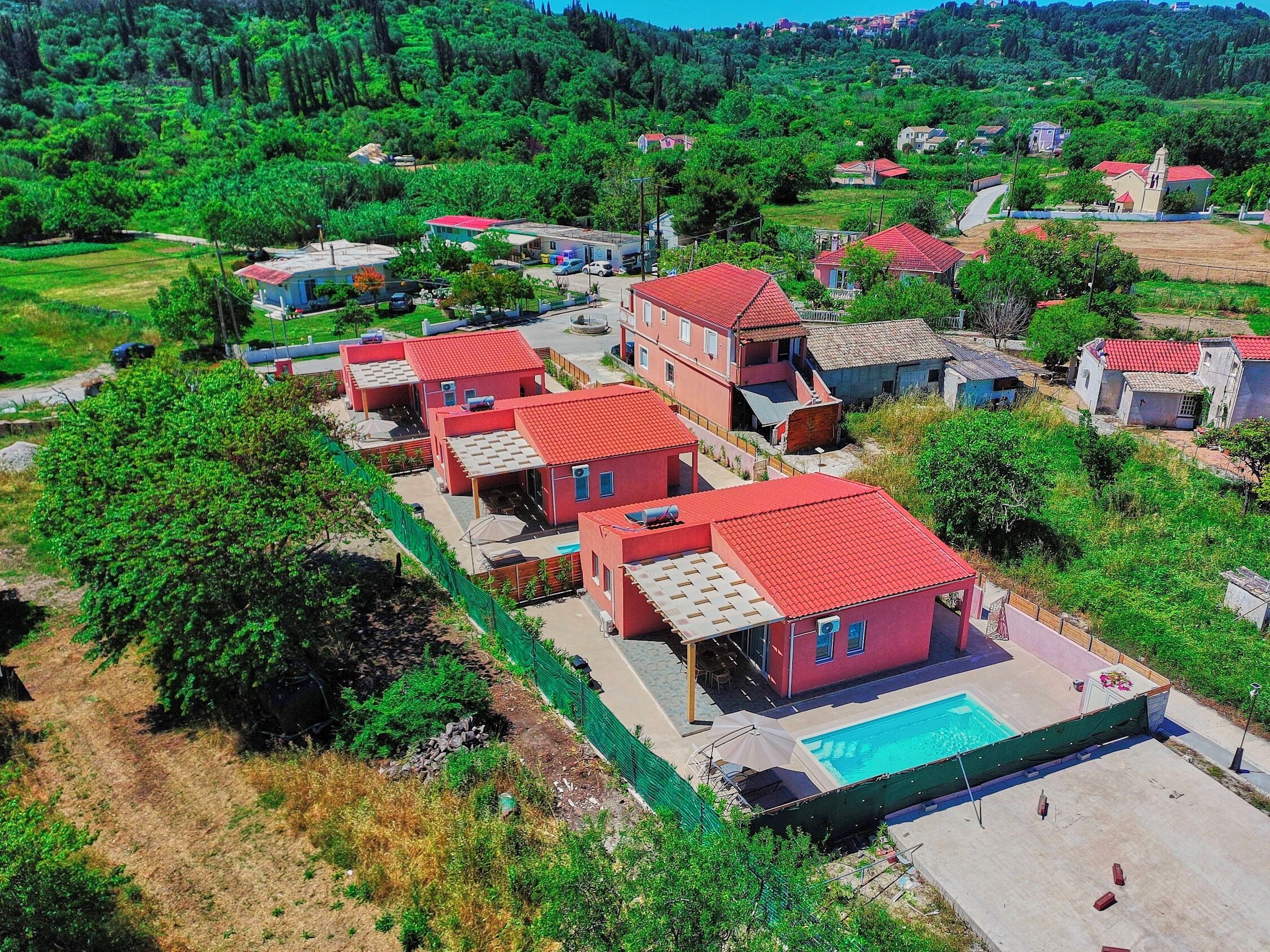 Zona residencial con varias casas de techo rojo, una piscina y abundante vegetación.