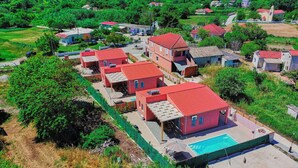 A residential area with multiple red-roofed houses, a swimming pool, and surrounding greenery. - Drastis Escape Villas - Villa Simran, By Estia (Peroulades)