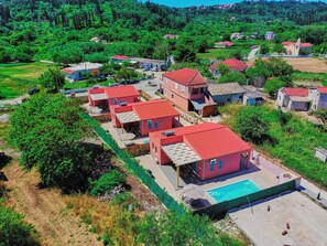 A residential area with multiple red-roofed houses, a swimming pool, and surrounding greenery. - Drastis Escape Villas - Villa Simran, By Estia (Peroulades)