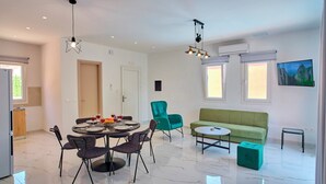 A modern living room with a dining area, green sofa, and a TV on the wall. - Drastis Escape Villas - Villa Simran, By Estia (Peroulades)
