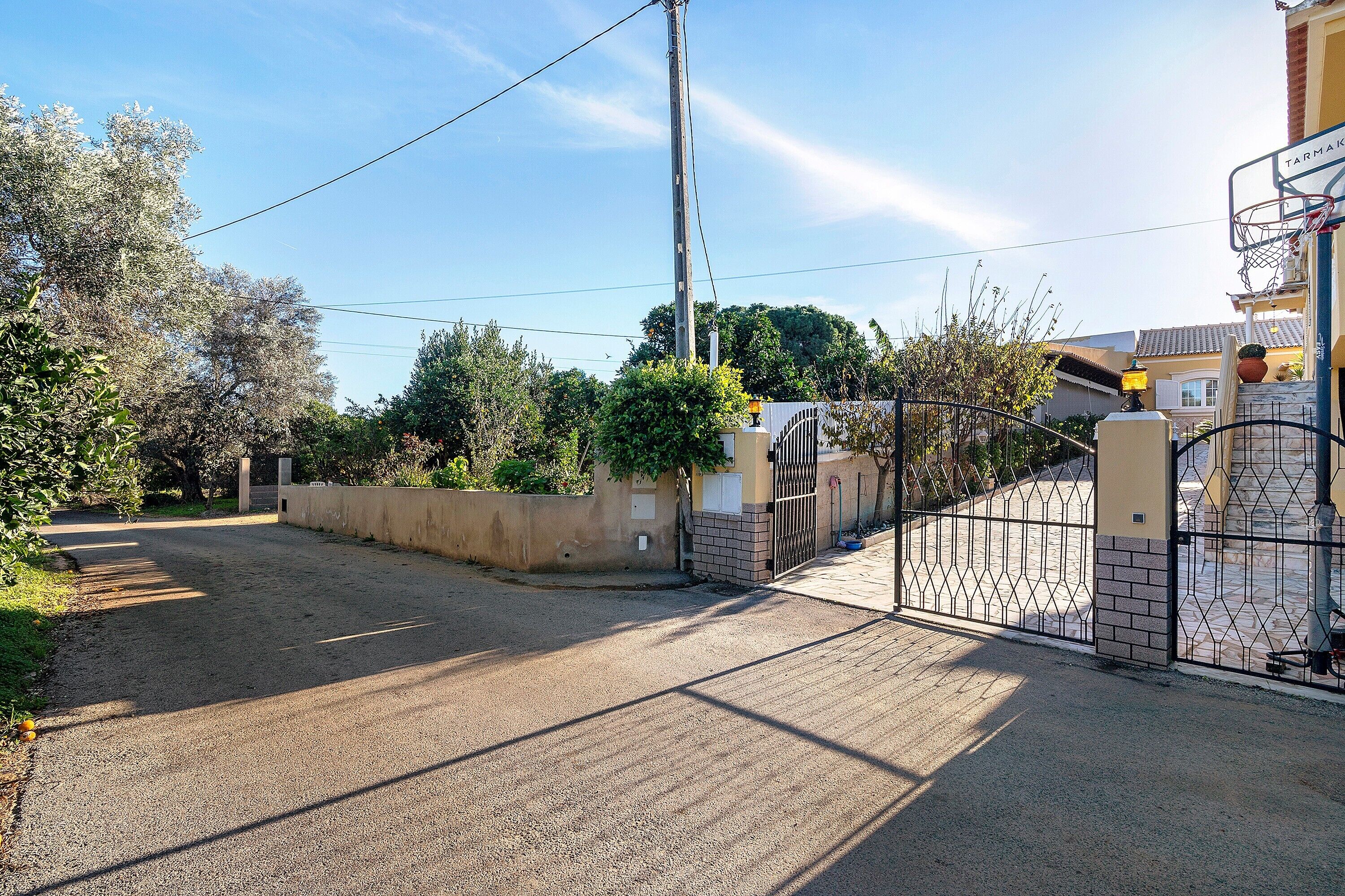 A residential street with a gated entrance, a basketball hoop, and a clear sky.