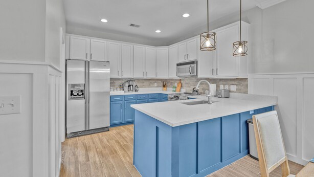 Une cuisine moderne avec des meubles blancs, un îlot central bleu, des appareils en acier inoxydable et des luminaires suspendus.