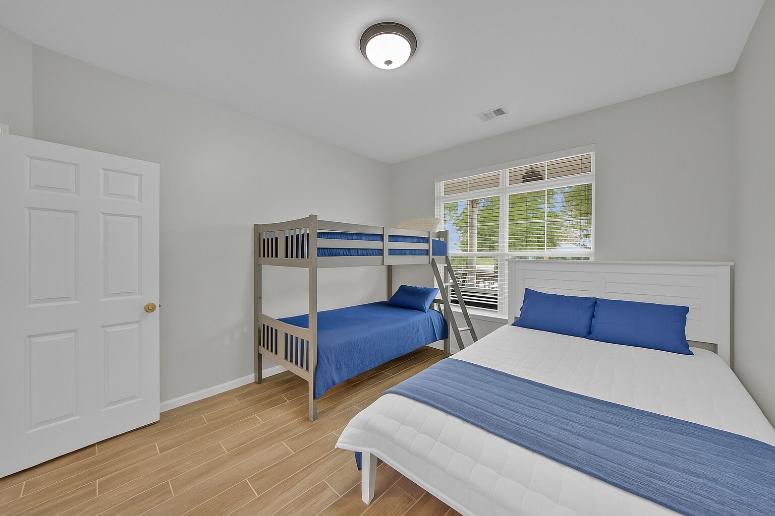 A bedroom with a bunk bed, a single bed, a window with blinds, and a door.