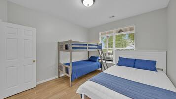 A bedroom with a bunk bed, a single bed, a window with blinds, and a door.