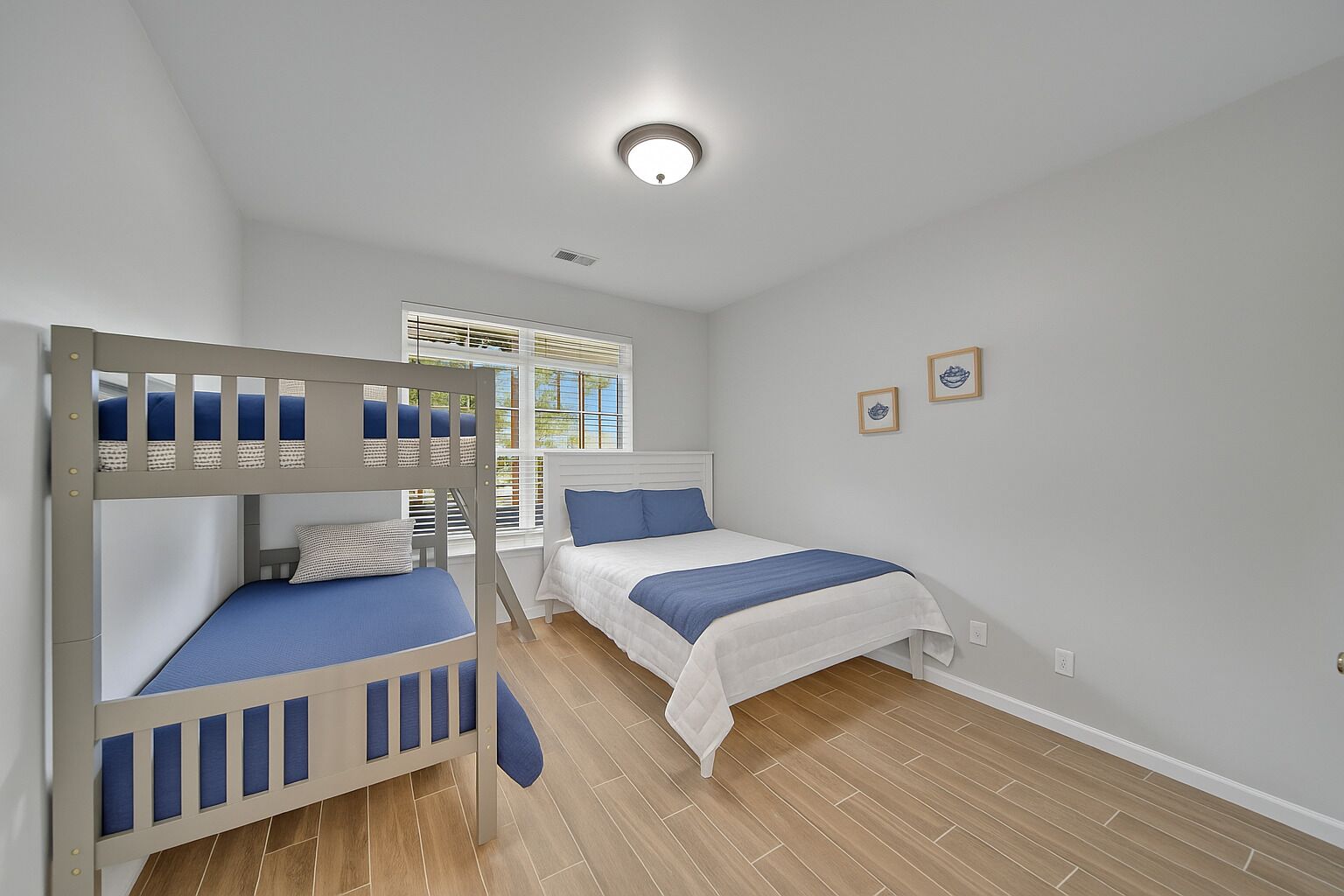 A bedroom with two bunk beds, a window with blinds, and a ceiling light.