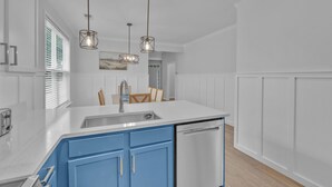 Une cuisine moderne avec des meubles blancs, un mur d’accent bleu et des luminaires suspendus.