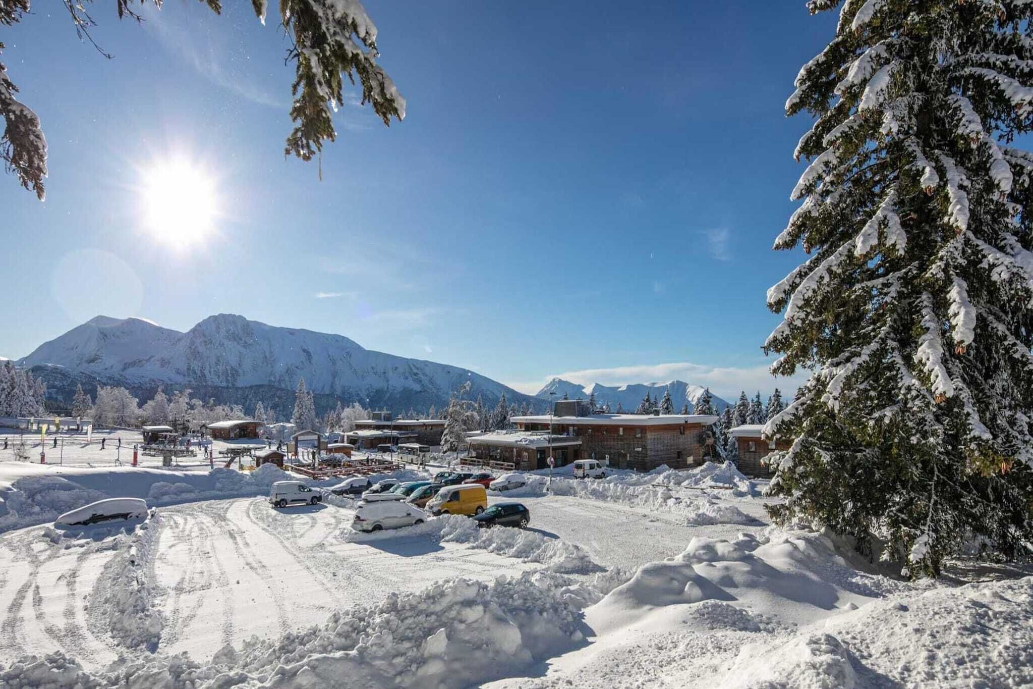 Een besneeerd berglandschap met heldere lucht, een parkeerplaats met meerdere auto's, en gebouwen met sneeuw bedekte daken.