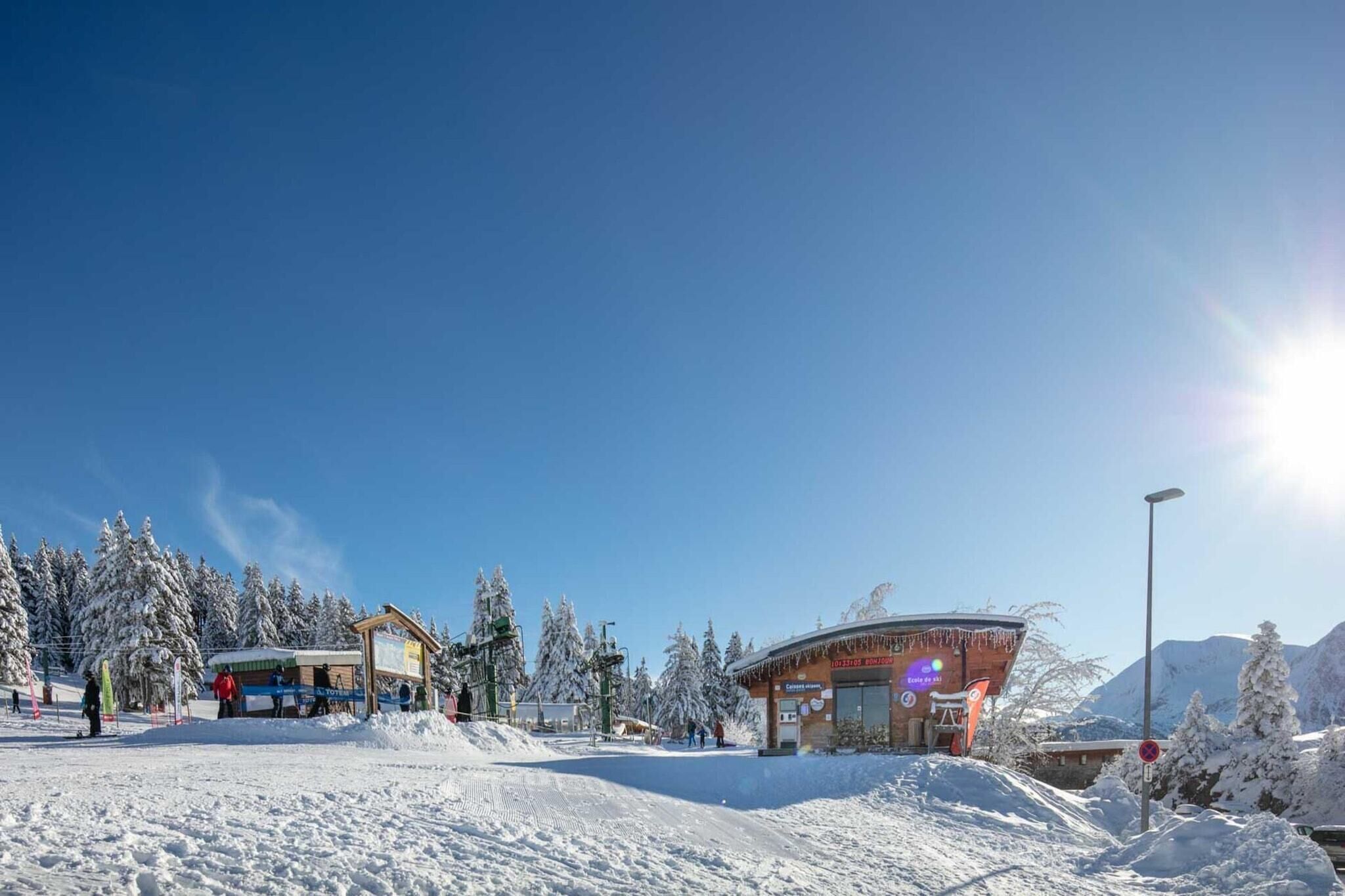 Estación de esquí cubierta de nieve con telesilla, un pequeño edificio con un letrero y árboles nevados.