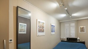 Habitació d'hotel amb un llit gran, una taula de nit amb una làmpada, un mirall i tres quadres a la paret.