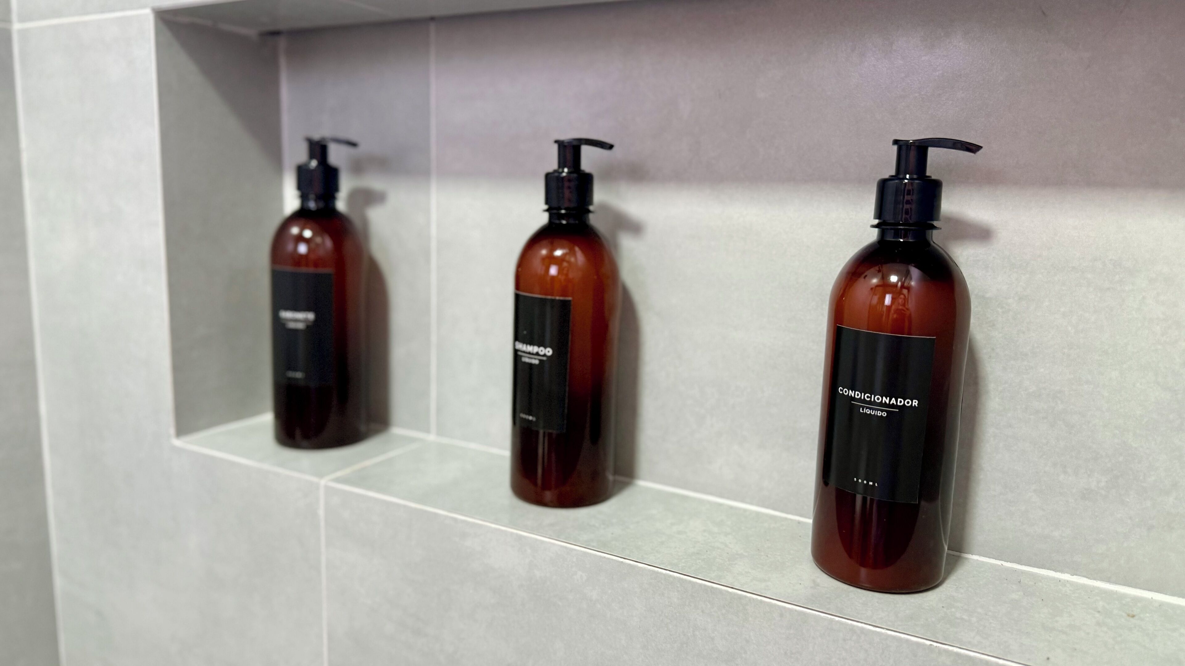 Tres botellas de champú y acondicionador sobre una estantería de azulejos.