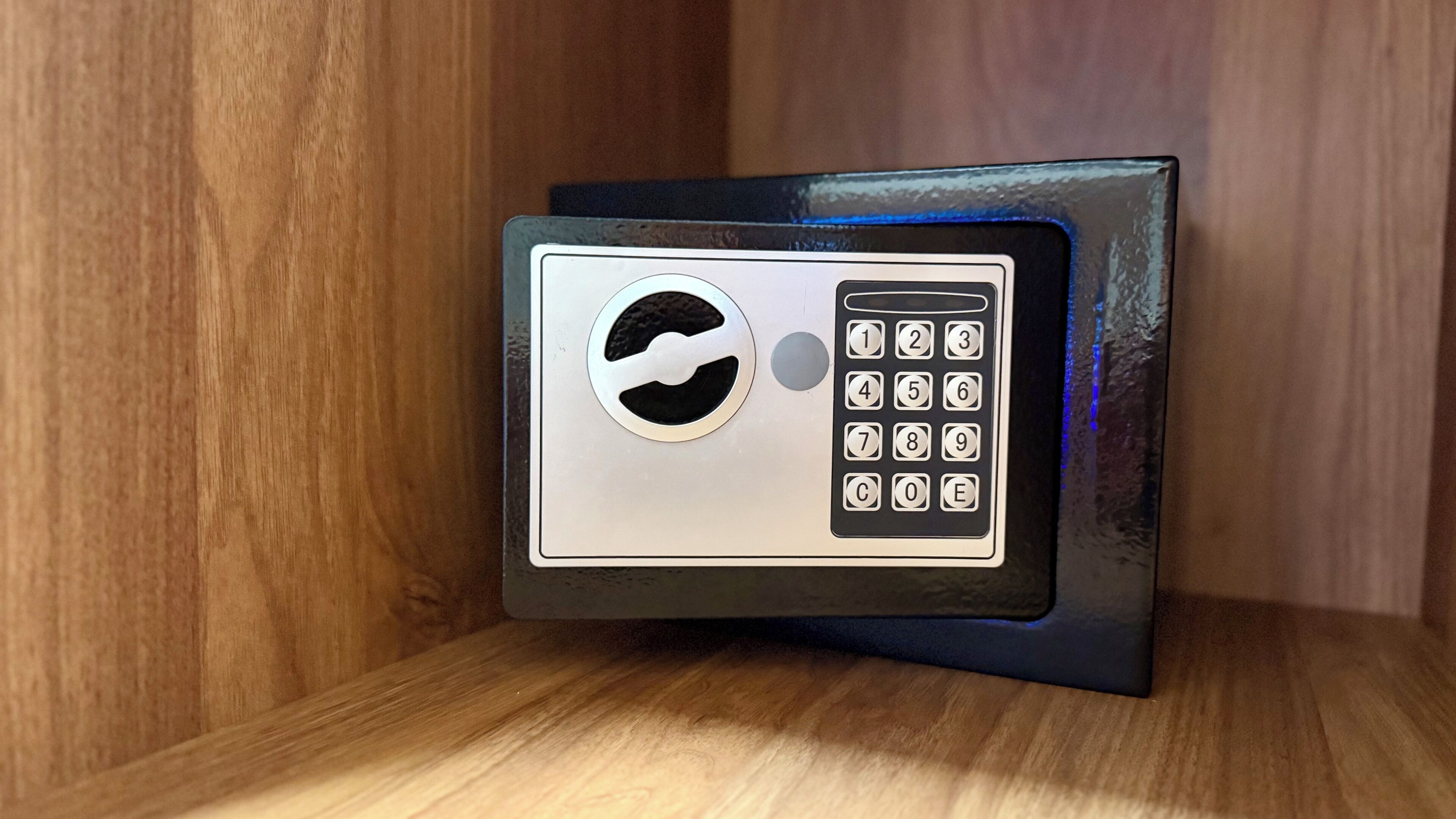Een metalen kluis met een keypad, geplaatst op een houten plank.