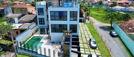 A modern two-story building with a swimming pool, a car, and a truck parked in front.