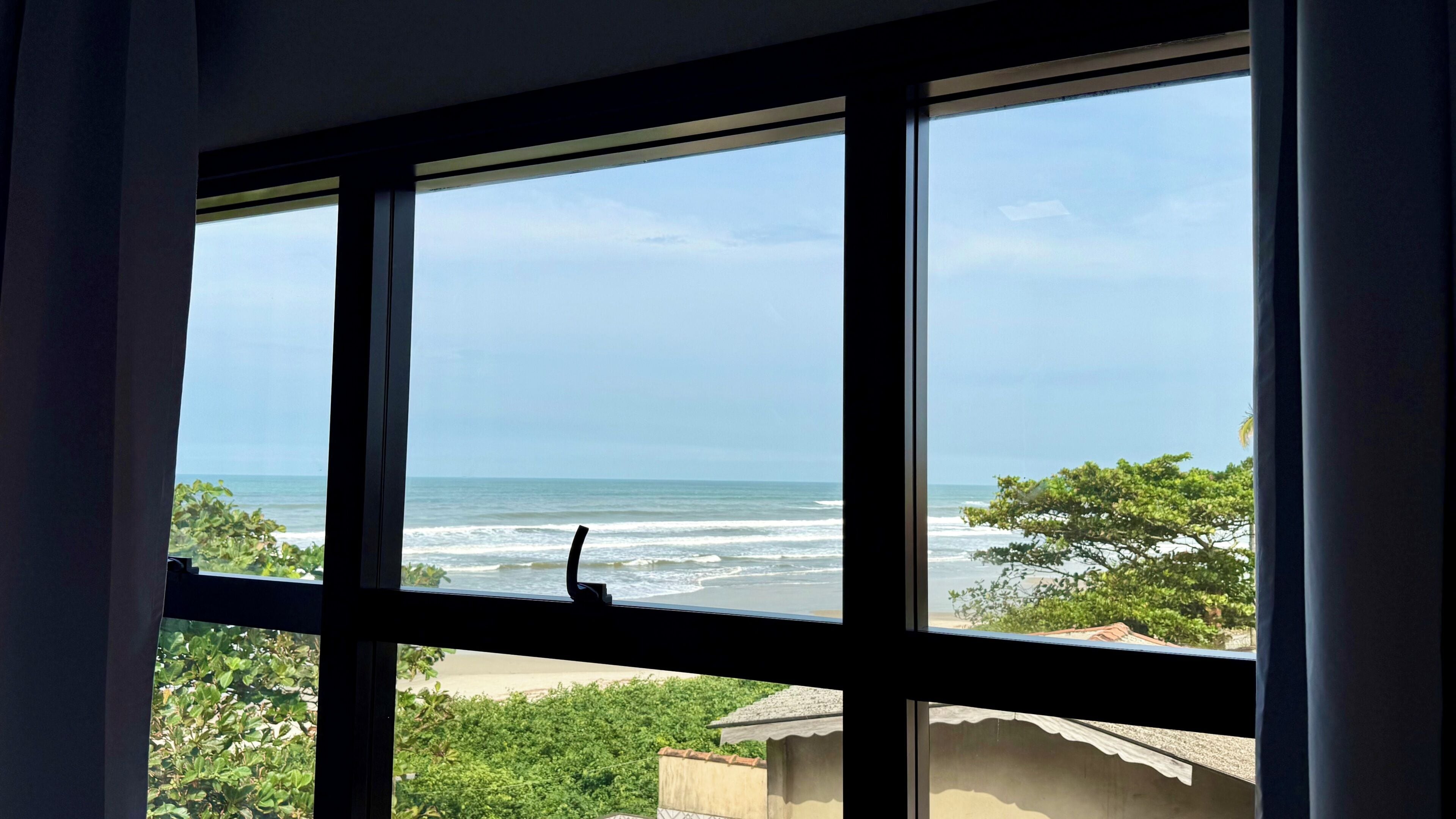 A window with a view of the ocean and greenery.