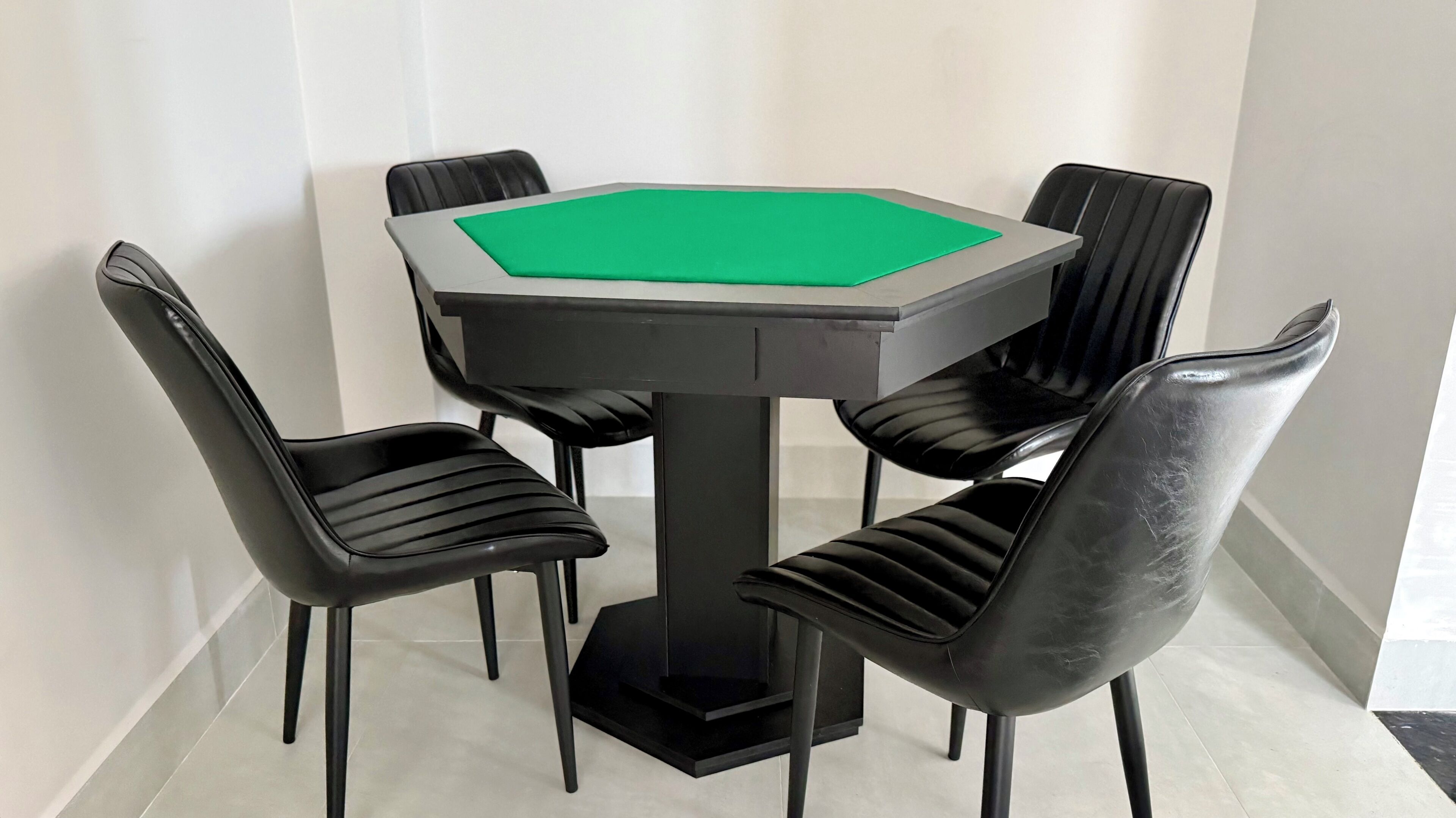 A round table with a green playing surface, surrounded by four black chairs with a modern design.
