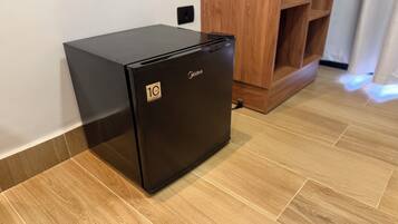 Un refrigerador negro con una etiqueta que indica una garantía de 10 años, sobre un piso de madera junto a una pared blanca y un mueble de madera.
