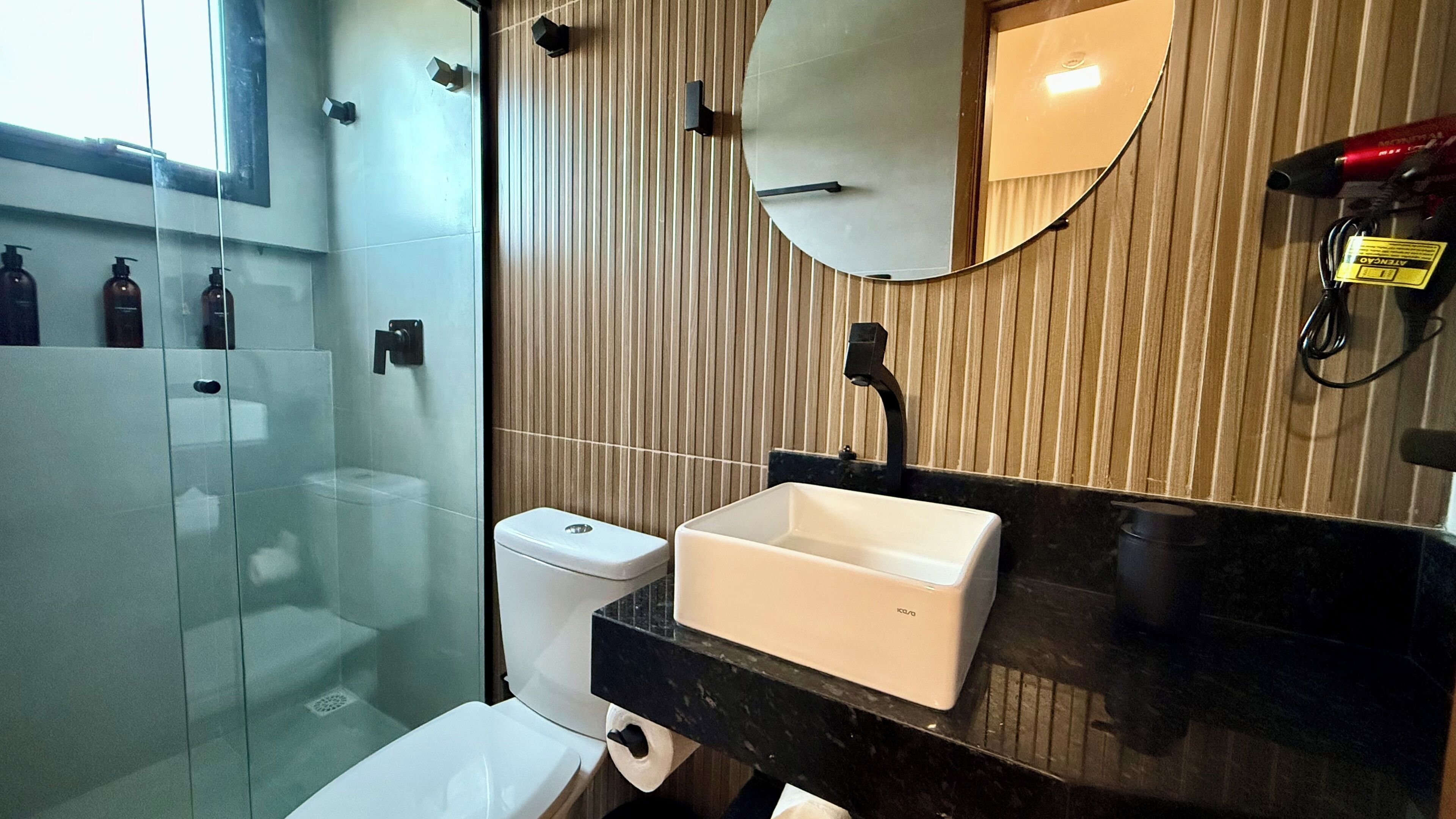 Uma casa de banho moderna com cabine de chuveiro em vidro, sanita branca e lavatório preto com espelho em cima.